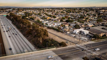 Overhead drone shot of the 105 freeway at sunset, next to houses in South Los Angeles