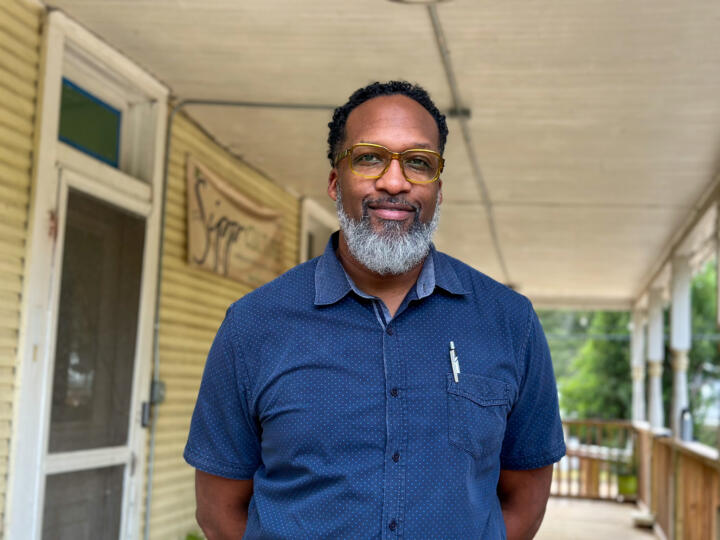 Photograph of Carlton Turner, a Black man sporting glasses, a gray beard, and a dark blue short-sleeve button-down shirt