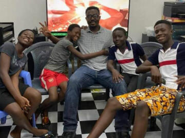 Photo of Elijah Newman on a couch surrounded by four of his children in Ghana