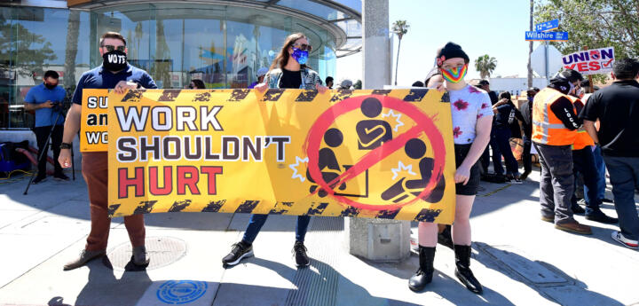 Three people hold up a sign that says "Work shouldn't hurt" at a protest in front of a Fidelity investments building.