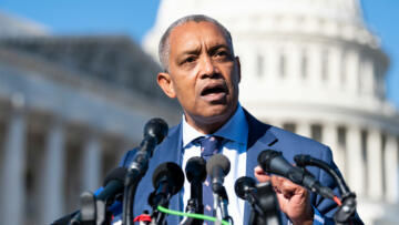 D.C. Attorney General Karl Racine standing at a podium with microphones.