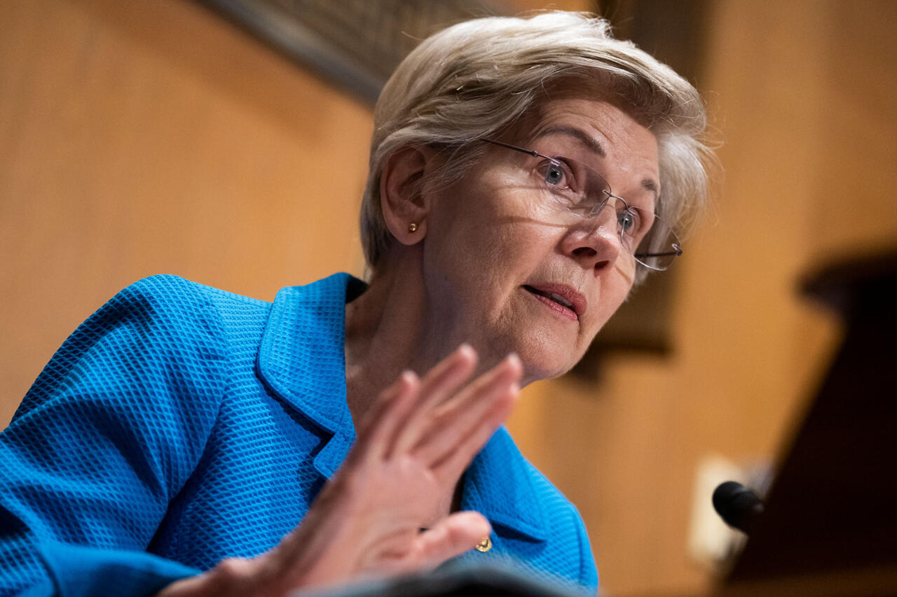 Photograph of Senator Elizabeth Warren at a podium. She is wearing glasses and a blue blazer.