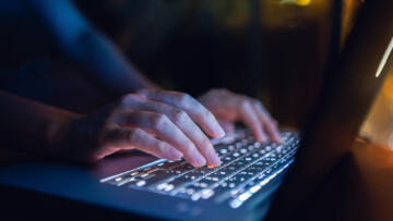 Photograph of a closeup of hands typing on a laptop.