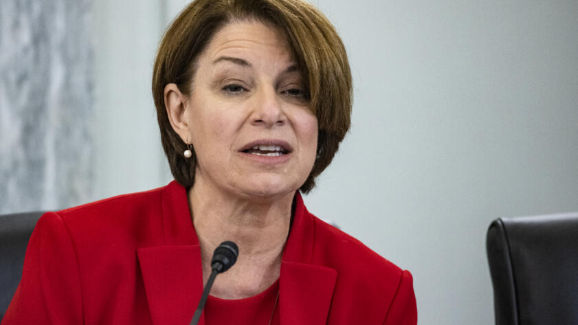 Photo of Amy Klobuchar in red suit before a microphone