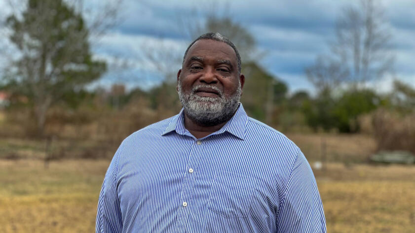 Photograph of Obbie Riley, a Black man sporting a grey beard and a blue button-down shirt