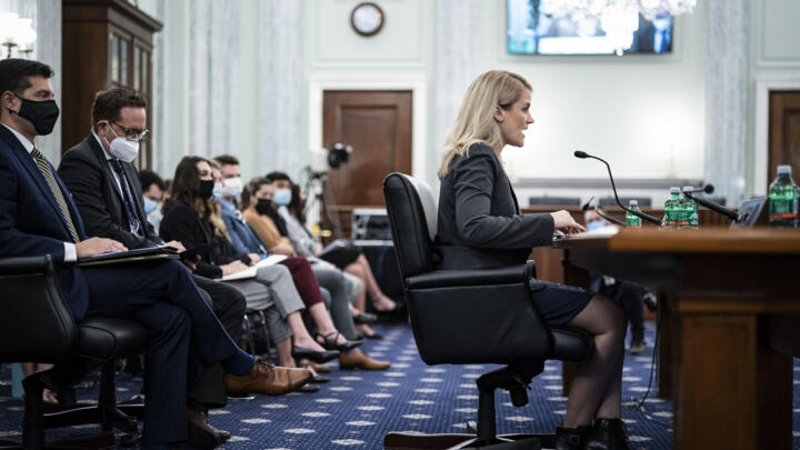 Frances Haugen sits at a table speaking into a microphone.