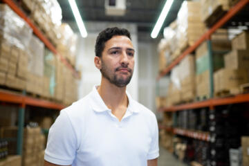 Photograph of a man in a white polo shirt standing in a warehouse.