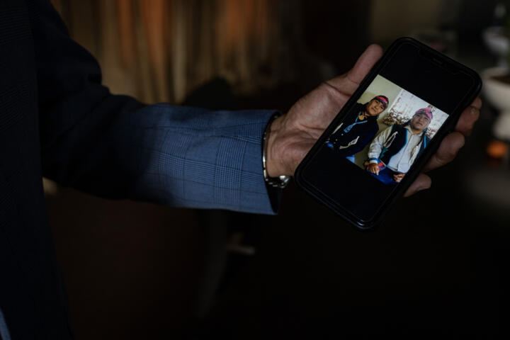 Close-up photograph of Lee Yaiva’s hand holding a smartphone displaying a photograph of his two brothers