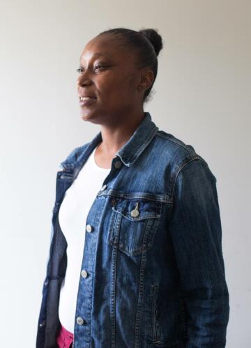 Photograph of Chantel Jones, a Black woman wearing a denim jacket. She is standing and looking off to the side, with a slight smile.