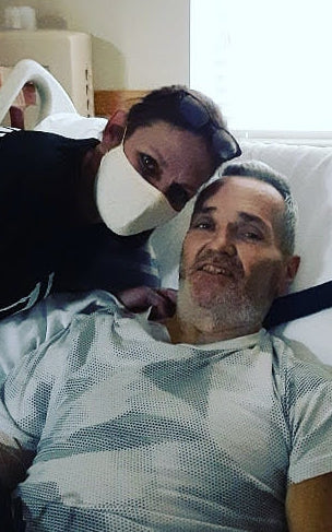 Photo of masked Sheryl Cross leaning over Tommy in hospital bed